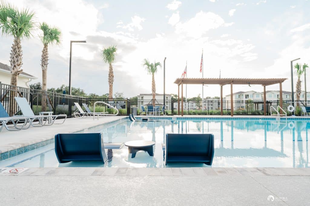 Apartments in Ocala with a swimming pool surrounded by lounge chairs and palm trees.