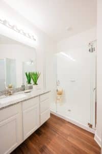 Apartments for rent in Ocala Bright modern bathroom with a glass-enclosed shower, white vanity, and hardwood floor. Aurora St. Leon Apartments in Ocala 2150 NW 21st Avenue | Ocala, FL 34475 (352) 233-4133