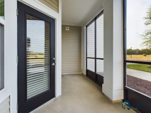Apartments for rent in Ocala Residential entryway featuring a black front door with blinds between glass panels, leading to a covered porch area with a view of the outdoor surroundings of two bedroom apartments in Ocala. Aurora St. Leon Apartments in Ocala 2150 NW 21st Avenue | Ocala, FL 34475 (352) 233-4133