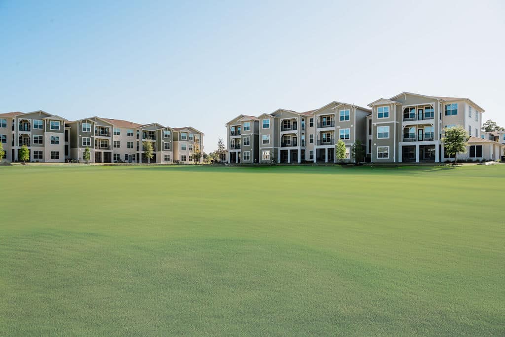 Apartments for rent in Ocala Wide grassy field in front of rows of modern three-story apartment buildings under a clear blue sky. Aurora St. Leon Apartments in Ocala 2150 NW 21st Avenue | Ocala, FL 34475 (352) 233-4133