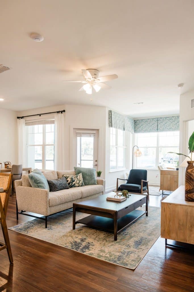 Apartments for rent in Ocala A modern living room with a beige sofa, wooden coffee table, blue accent chair, and large windows letting in natural light. A ceiling fan is on the white ceiling, and the floor is hardwood. Aurora St. Leon Apartments in Ocala 2150 NW 21st Avenue | Ocala, FL 34475 (352) 233-4133