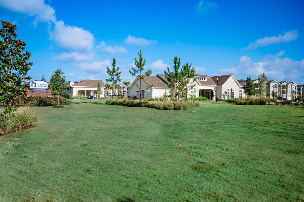 Apartments for rent in Ocala A grassy field in front of a residential property with a sign on the left reading "Natura." Several buildings and trees are visible against a blue sky. Aurora St. Leon Apartments in Ocala 2150 NW 21st Avenue | Ocala, FL 34475 (352) 233-4133