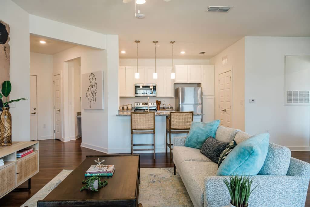 Apartments for rent in Ocala A modern living room with a sofa, coffee table, and kitchen in the background. The kitchen has an island with two barstools, pendant lighting, and stainless steel appliances. Aurora St. Leon Apartments in Ocala 2150 NW 21st Avenue | Ocala, FL 34475 (352) 233-4133