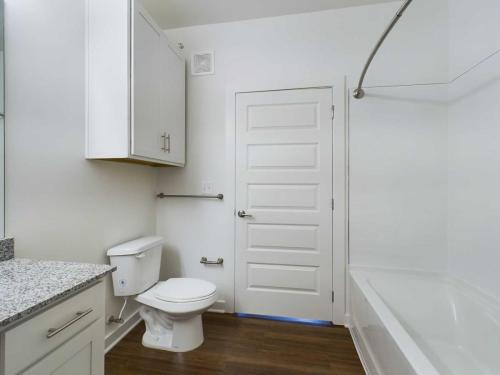 Apartments for rent in Ocala A modern bathroom with white walls, a white toilet, a bathtub with a curved shower rod, a granite countertop, and wooden flooring. Aurora St. Leon Apartments in Ocala 2150 NW 21st Avenue | Ocala, FL 34475 (352) 233-4133