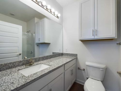 Apartments for rent in Ocala Modern bathroom with granite countertop, single sink, large mirror, and white cabinets. It includes a toilet and a glass-enclosed shower. Overhead lighting features multiple bulbs. Aurora St. Leon Apartments in Ocala 2150 NW 21st Avenue | Ocala, FL 34475 (352) 233-4133