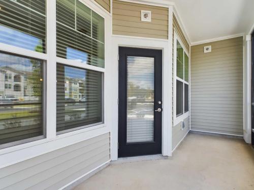 Apartments for rent in Ocala An outdoor patio area with a light-colored floor, beige wood-paneled walls, and large windows with blinds. A black-framed door with a glass panel is in the center. Aurora St. Leon Apartments in Ocala 2150 NW 21st Avenue | Ocala, FL 34475 (352) 233-4133
