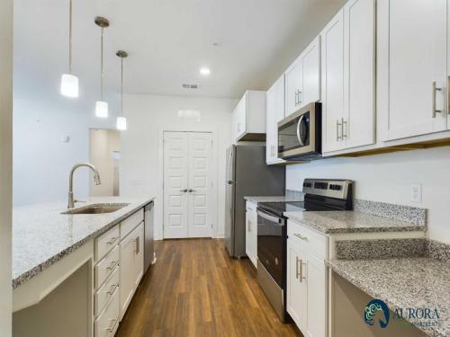 Apartments for rent in Ocala A modern kitchen featuring white cabinets, stainless steel appliances, a granite countertop island with a sink, and pendant lighting. Aurora St. Leon Apartments in Ocala 2150 NW 21st Avenue | Ocala, FL 34475 (352) 233-4133