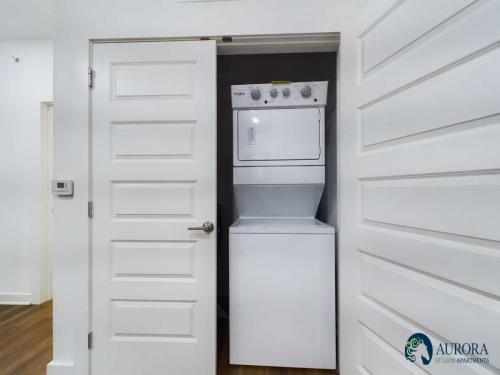 Apartments for rent in Ocala A stacked washer and dryer unit is visible in a small closet with white paneled doors partially open, exposing the appliances. Aurora St. Leon Apartments logo is displayed at the bottom right corner. Aurora St. Leon Apartments in Ocala 2150 NW 21st Avenue | Ocala, FL 34475 (352) 233-4133
