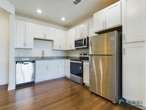 Apartments for rent in Ocala A modern kitchen with white cabinets, stainless steel appliances including a refrigerator, microwave, oven, and dishwasher, and a granite countertop with a sink. The flooring is hardwood. Aurora St. Leon Apartments in Ocala 2150 NW 21st Avenue | Ocala, FL 34475 (352) 233-4133