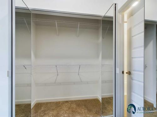 Apartments for rent in Ocala Empty closet with mirrored sliding doors, white walls, and beige carpet. Shelves and hanging bars are installed. A door is partially visible to the right. Aurora St. Leon Apartments logo is in the bottom right. Aurora St. Leon Apartments in Ocala 2150 NW 21st Avenue | Ocala, FL 34475 (352) 233-4133
