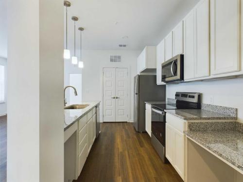Apartments for rent in Ocala Modern kitchen with wooden floors, white cabinets, stainless steel appliances including a microwave, oven, and refrigerator, granite countertops, and a central island with pendant lighting. Aurora St. Leon Apartments in Ocala 2150 NW 21st Avenue | Ocala, FL 34475 (352) 233-4133