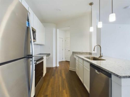 Apartments for rent in Ocala Modern kitchen with stainless steel appliances, granite countertops, white cabinetry, and wooden flooring. Pendant lights hang over the island with a built-in sink and dishwasher. Aurora St. Leon Apartments in Ocala 2150 NW 21st Avenue | Ocala, FL 34475 (352) 233-4133