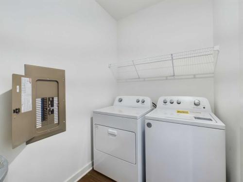 Apartments for rent in Ocala Laundry room with a washer, a dryer, a metal shelf above them, and an open electrical panel on the wall. Aurora St. Leon Apartments in Ocala 2150 NW 21st Avenue | Ocala, FL 34475 (352) 233-4133