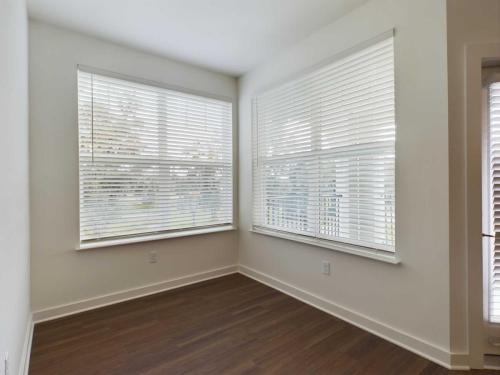 Apartments for rent in Ocala A small, empty room with white walls, large windows with white blinds, and dark wood flooring. Sunlight is filtering through the blinds. Aurora St. Leon Apartments in Ocala 2150 NW 21st Avenue | Ocala, FL 34475 (352) 233-4133