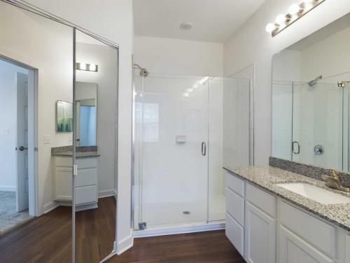 Apartments for rent in Ocala Modern bathroom with a glass-enclosed shower, granite countertop on the vanity, mirrored closet doors, and wooden flooring. Aurora St. Leon Apartments in Ocala 2150 NW 21st Avenue | Ocala, FL 34475 (352) 233-4133