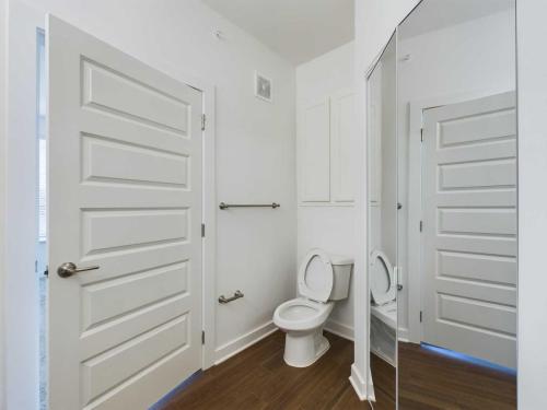 Apartments for rent in Ocala A modern bathroom with a white toilet, a large mirror, a closed door, a towel bar, and a hardwood floor. Aurora St. Leon Apartments in Ocala 2150 NW 21st Avenue | Ocala, FL 34475 (352) 233-4133