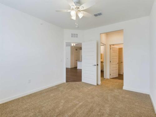 Apartments for rent in Ocala A carpeted bedroom with white walls, a ceiling fan, and two open doors leading to a hallway and a bathroom. Aurora St. Leon Apartments in Ocala 2150 NW 21st Avenue | Ocala, FL 34475 (352) 233-4133