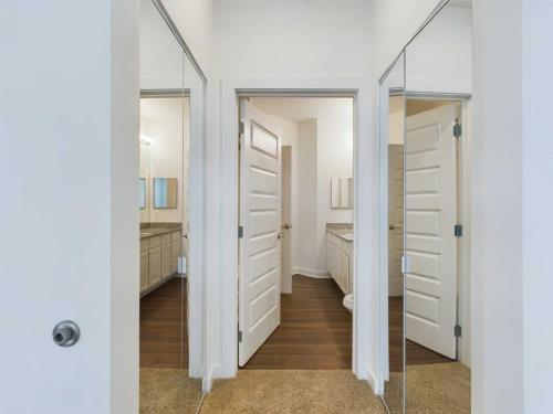 Apartments for rent in Ocala A hallway with two mirrored closet doors on either side leads to a bathroom with white cabinets, a granite countertop, and a wooden floor. The partially open white door provides a view of the bathroom. Aurora St. Leon Apartments in Ocala 2150 NW 21st Avenue | Ocala, FL 34475 (352) 233-4133