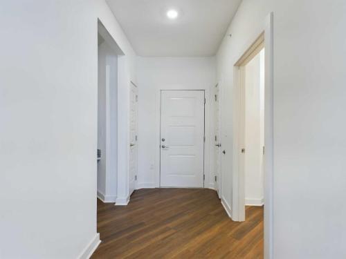 Apartments for rent in Ocala White hallway with wooden flooring, a closed white entrance door at the center, and open doorways on both sides. Aurora St. Leon Apartments in Ocala 2150 NW 21st Avenue | Ocala, FL 34475 (352) 233-4133