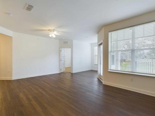 Apartments for rent in Ocala Empty room with white walls, large windows with blinds, wood flooring, ceiling fan, and a partially open door. Aurora St. Leon Apartments in Ocala 2150 NW 21st Avenue | Ocala, FL 34475 (352) 233-4133
