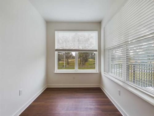Apartments for rent in Ocala Empty room with white walls, wooden floor, and large windows with white blinds. The windows overlook a green outdoor area. Aurora St. Leon Apartments in Ocala 2150 NW 21st Avenue | Ocala, FL 34475 (352) 233-4133