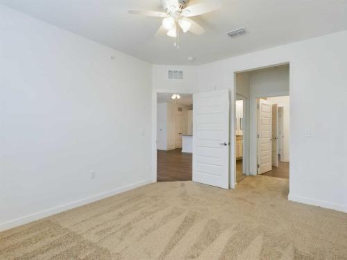 Apartments for rent in Ocala Empty bedroom with beige carpet, white walls, ceiling fan, and open doors leading to a bathroom and hallway. Aurora St. Leon Apartments in Ocala 2150 NW 21st Avenue | Ocala, FL 34475 (352) 233-4133
