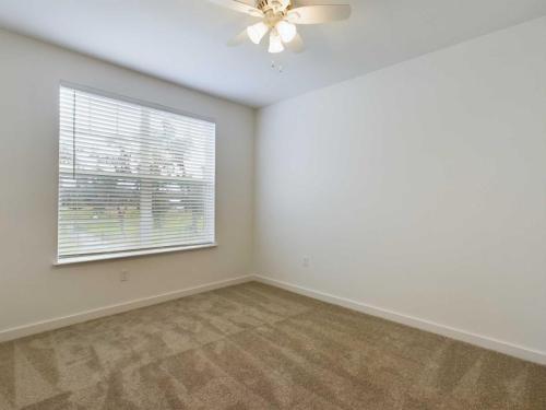 Apartments for rent in Ocala An empty room with beige carpet, a white ceiling fan, and a large window with blinds. The walls and ceiling are painted white. Aurora St. Leon Apartments in Ocala 2150 NW 21st Avenue | Ocala, FL 34475 (352) 233-4133