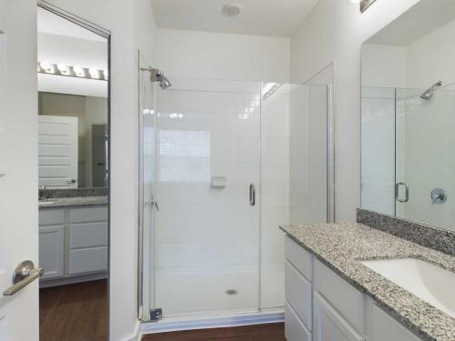 Apartments for rent in Ocala A modern bathroom featuring a glass-enclosed shower, a granite countertop with a sink, white cabinets, and a large wall mirror with lighting above it. The floor is covered with dark wood. Aurora St. Leon Apartments in Ocala 2150 NW 21st Avenue | Ocala, FL 34475 (352) 233-4133