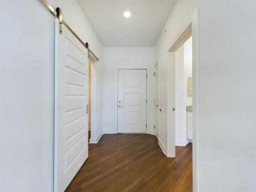 Apartments for rent in Ocala White-walled hallway with wooden flooring, featuring three open doors, a sliding door on the left, and a closed door at the end. Ceiling light is on. Aurora St. Leon Apartments in Ocala 2150 NW 21st Avenue | Ocala, FL 34475 (352) 233-4133