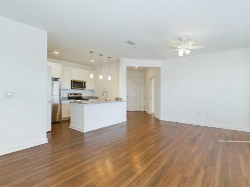 Apartments for rent in Ocala A modern kitchen and living area with wooden flooring, white walls, a ceiling fan, stainless steel appliances, an island with pendant lights, and a door in the background. Aurora St. Leon Apartments in Ocala 2150 NW 21st Avenue | Ocala, FL 34475 (352) 233-4133