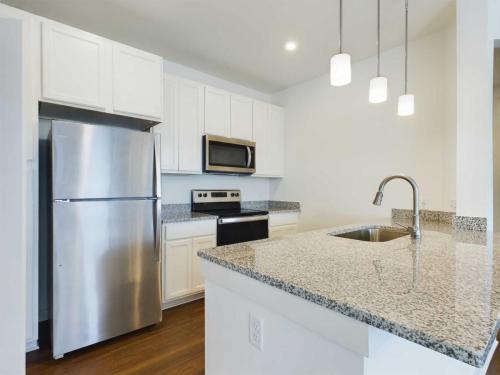 Apartments for rent in Ocala Modern kitchen with stainless steel appliances, white cabinets, granite countertops, and a large island with a sink. Three pendant lights hang above the island. Aurora St. Leon Apartments in Ocala 2150 NW 21st Avenue | Ocala, FL 34475 (352) 233-4133