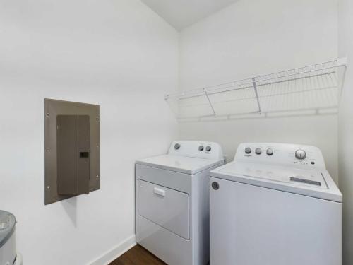 Apartments for rent in Ocala A laundry room with a white washing machine and dryer set, a metal utility box on the wall, and a wire shelf above the appliances. Aurora St. Leon Apartments in Ocala 2150 NW 21st Avenue | Ocala, FL 34475 (352) 233-4133