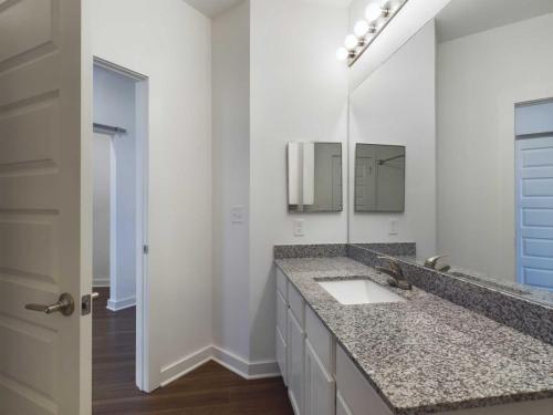 Apartments for rent in Ocala Modern bathroom featuring a long granite countertop with a white sink, large mirror, and a set of vanity lights above. Doorways on the left and right lead to adjacent rooms. Aurora St. Leon Apartments in Ocala 2150 NW 21st Avenue | Ocala, FL 34475 (352) 233-4133