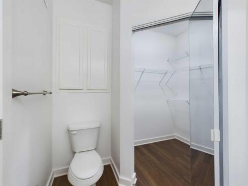 Apartments for rent in Ocala Image of a small bathroom with a white toilet next to a walk-in closet that has wooden flooring and white wire shelves. Aurora St. Leon Apartments in Ocala 2150 NW 21st Avenue | Ocala, FL 34475 (352) 233-4133