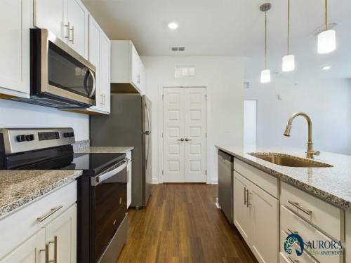 Apartments for rent in Ocala Modern kitchen with white cabinets, granite countertops, stainless steel appliances, and a center island with a sink and faucet. The room has wooden flooring and a double-door pantry. Aurora St. Leon Apartments in Ocala 2150 NW 21st Avenue | Ocala, FL 34475 (352) 233-4133