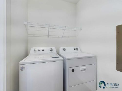 Apartments for rent in Ocala A compact laundry room with a white top-loading washing machine and a white front-loading dryer beneath a white wire shelf. Aurora St. Leon Apartments in Ocala 2150 NW 21st Avenue | Ocala, FL 34475 (352) 233-4133