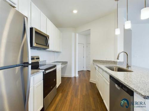 Apartments for rent in Ocala Modern kitchen with stainless steel appliances, white cabinets, granite countertops, dark hardwood flooring, and pendant lighting over a sink with a logo saying "Aurora Glen Apartments" in the corner. Aurora St. Leon Apartments in Ocala 2150 NW 21st Avenue | Ocala, FL 34475 (352) 233-4133