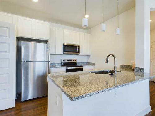 Apartments for rent in Ocala Modern kitchen with white cabinets, stainless steel appliances including a refrigerator, oven, and microwave, granite countertops, sink with a faucet, and two pendant lights over the island. Aurora St. Leon Apartments in Ocala 2150 NW 21st Avenue | Ocala, FL 34475 (352) 233-4133
