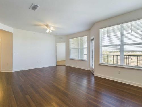 Apartments for rent in Ocala An empty room with wooden floors, white walls, large windows, a ceiling fan, and an open doorway. Aurora St. Leon Apartments in Ocala 2150 NW 21st Avenue | Ocala, FL 34475 (352) 233-4133