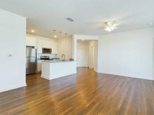 Apartments for rent in Ocala Spacious open-concept kitchen and living area with wood flooring, white cabinets, stainless steel appliances, ceiling fan, and natural light from multiple windows. Aurora St. Leon Apartments in Ocala 2150 NW 21st Avenue | Ocala, FL 34475 (352) 233-4133