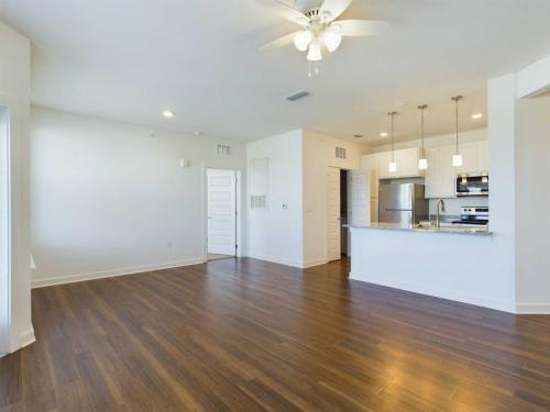 Apartments for rent in Ocala Spacious, empty living area with hardwood floors, white walls, ceiling fan, and a modern kitchen featuring white cabinets, stainless steel appliances, and a breakfast bar. Aurora St. Leon Apartments in Ocala 2150 NW 21st Avenue | Ocala, FL 34475 (352) 233-4133
