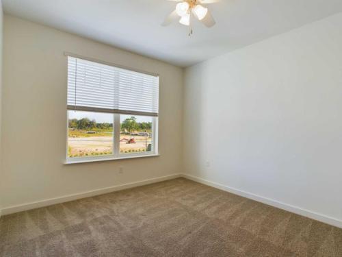 Apartments for rent in Ocala An empty room with beige carpet, a ceiling fan, and a window with blinds, showing a view of a construction site outside. Aurora St. Leon Apartments in Ocala 2150 NW 21st Avenue | Ocala, FL 34475 (352) 233-4133