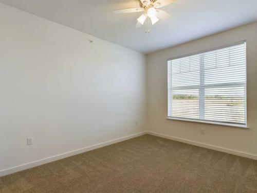Apartments for rent in Ocala A vacant room with beige carpet, white walls, a ceiling fan with lights, and a window with horizontal blinds allowing natural light to enter. Aurora St. Leon Apartments in Ocala 2150 NW 21st Avenue | Ocala, FL 34475 (352) 233-4133