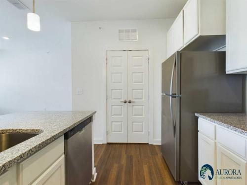 Apartments for rent in Ocala Modern kitchen featuring stainless steel appliances, granite countertops, white cabinets, and a wooden floor. Aurora Luxury Apartments logo in the lower right corner. Aurora St. Leon Apartments in Ocala 2150 NW 21st Avenue | Ocala, FL 34475 (352) 233-4133
