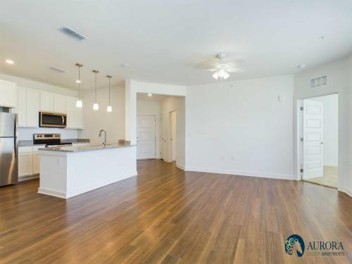 Apartments for rent in Ocala A modern, unfurnished apartment with wooden floors, white walls, an open kitchen with a large island, stainless steel appliances, and multiple doors leading to other rooms. Aurora St. Leon Apartments in Ocala 2150 NW 21st Avenue | Ocala, FL 34475 (352) 233-4133