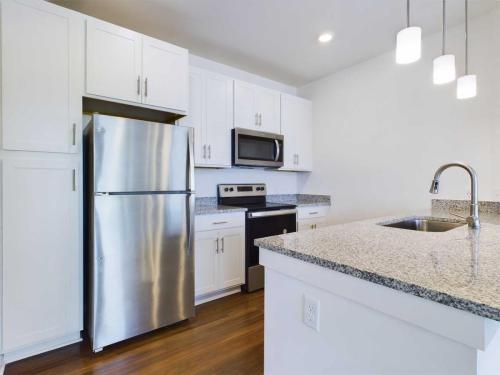 Apartments for rent in Ocala A modern kitchen with white cabinets, stainless steel refrigerator, oven, and microwave, granite countertops, sink with a faucet, and overhead pendant lights. Aurora St. Leon Apartments in Ocala 2150 NW 21st Avenue | Ocala, FL 34475 (352) 233-4133