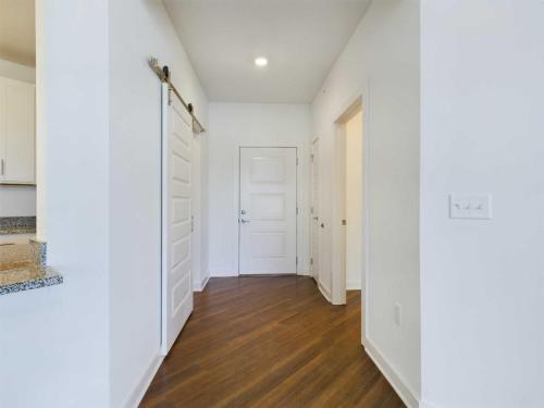 Apartments for rent in Ocala White-walled hallway with wooden flooring, featuring a closed door at the end, a partially open door on the right, and a sliding barn door on the left. Aurora St. Leon Apartments in Ocala 2150 NW 21st Avenue | Ocala, FL 34475 (352) 233-4133