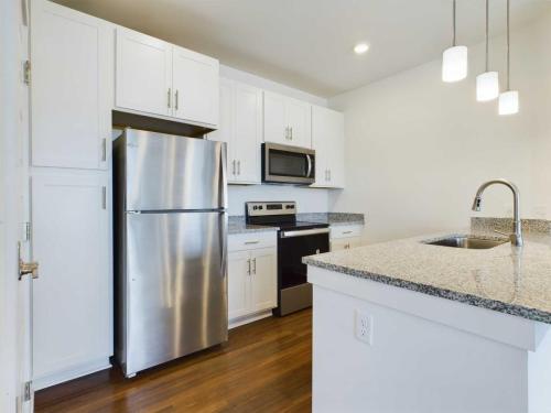Apartments for rent in Ocala Modern kitchen with stainless steel appliances, white cabinetry, granite countertops, and a kitchen island with a sink under pendant lights. Aurora St. Leon Apartments in Ocala 2150 NW 21st Avenue | Ocala, FL 34475 (352) 233-4133