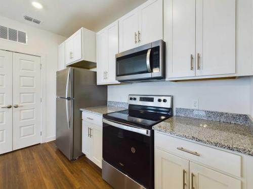 Apartments for rent in Ocala Modern kitchen with white cabinets, stainless steel refrigerator, microwave, and electric stove with oven. Granite countertops and wood flooring enhance the clean, contemporary design. Aurora St. Leon Apartments in Ocala 2150 NW 21st Avenue | Ocala, FL 34475 (352) 233-4133