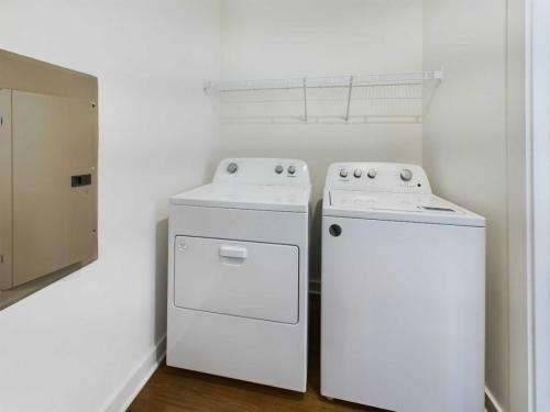 Apartments for rent in Ocala A laundry room with a white top-loading washing machine and a front-loading dryer placed side by side under a wire shelf. An electrical panel is mounted on the left wall. Aurora St. Leon Apartments in Ocala 2150 NW 21st Avenue | Ocala, FL 34475 (352) 233-4133